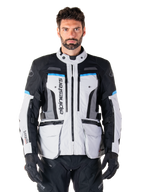 Alpinestars Bogota Pro Drystar Jacket, motocyklowa kurtka turystyczna adventure, kolor Ice Gray z czarnymi i błękitnymi akcentami, widok z przodu ukazujący panele wentylacyjne i kieszenie cargo, model w czarnych spodniach i rękawicach