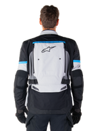 Kurtka Alpinestars Bogotá Pro Drystar®, motocyklowa kurtka adventure, kolor Ice Gray, czarny i cyjanowy, widok z tyłu przedstawiający duży jasnoszary panel z czarnym logo gwiazdy, cyjanowe akcenty z brandingiem Tech Touring oraz regulowane paski w talii