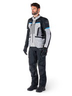 Motocyklista w kurtce Alpinestars Bogotá Pro Drystar® w kolorach Ice Gray, czarnym i cyjanowym, w zestawieniu z czarnymi technicznymi spodniami i rękawicami, odzież adventure touring zapewniająca wydajność w każdych warunkach pogodowych.