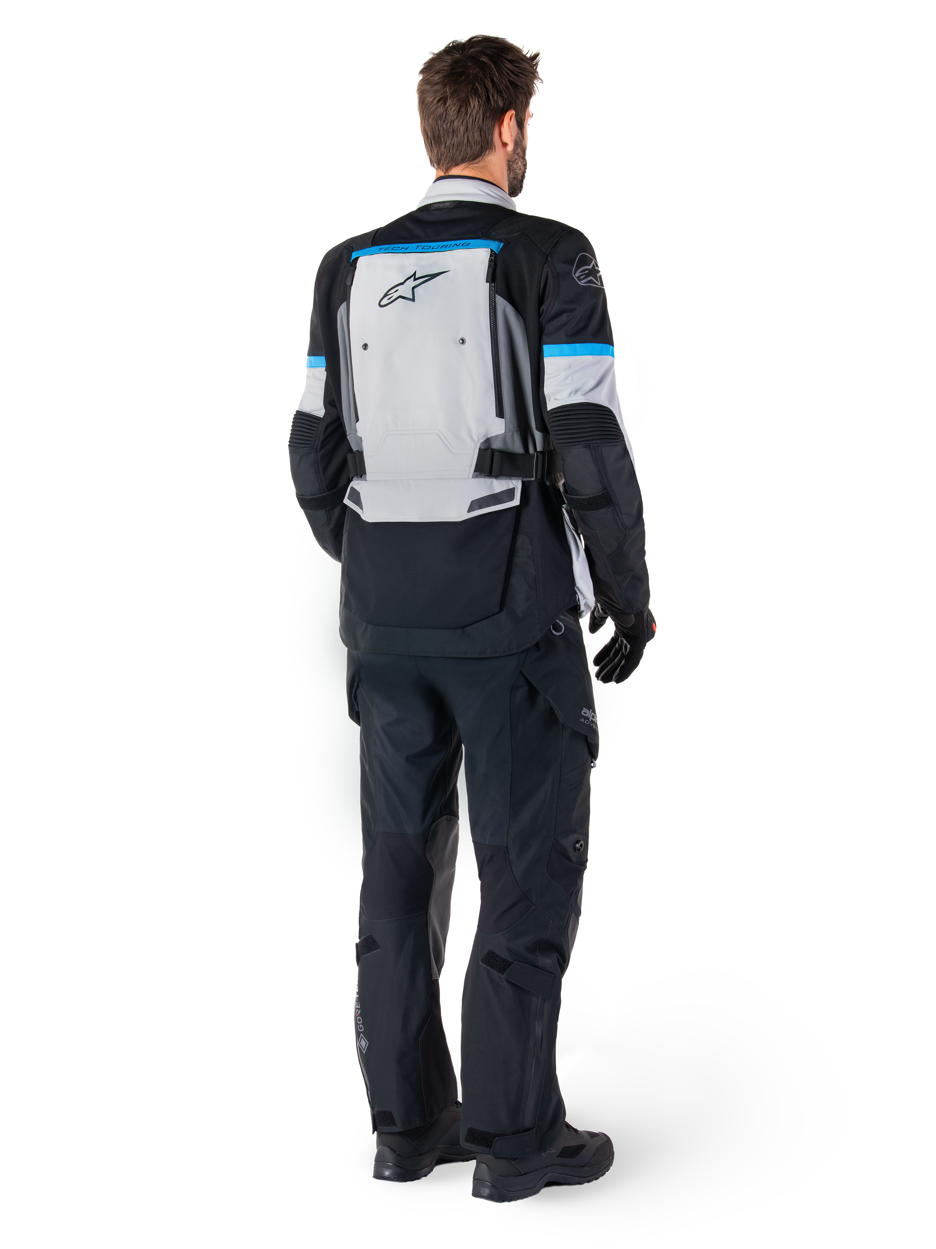 Kurtka Alpinestars Bogotá Pro Drystar®, motocyklowa kurtka adventure, kolor lodowy szary, czarny i cyjan, widok z tyłu z pasującymi czarnymi spodniami i rękawicami, duży szary panel na plecach z czarnym logo Alpinestars i błękitnymi akcentami.