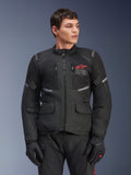 Alpinestars Andes Air Drystar® Jacket, czarna motocyklowa kurtka turystyczna, czerwone logo z gwiazdą na klatce piersiowej, panele wentylacyjne z siatki i odblaskowe akcenty, noszona przez męskiego modela w czarnych rękawicach, dwusezonowa odzież adventure