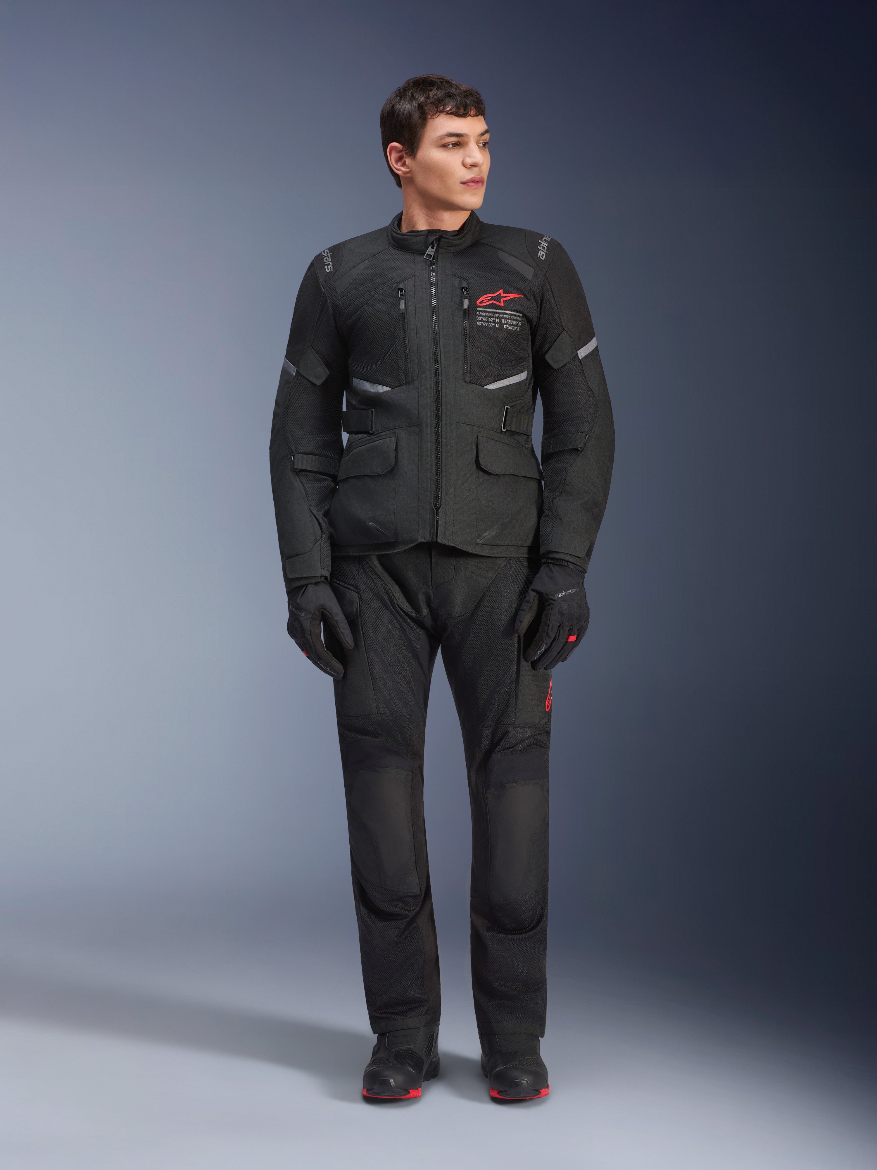Męski model w kurtce Alpinestars Andes Air Drystar® w kolorze czarnym, motocyklowy strój turystyczny adventure z dopasowanymi spodniami i rękawicami, czerwone logo na piersi, wentylacja siatkowa i funkcjonalne kieszenie