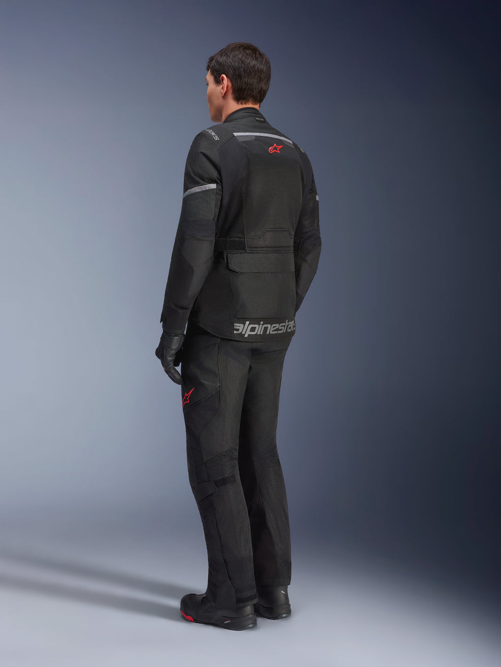 Spodnie Alpinestars Andes Air Drystar® i dopasowana kurtka, czarne z czerwonymi logotypami gwiazdy, motocyklowa odzież adventure touring widoczna od tyłu, z siatkowymi panelami wentylacyjnymi i odblaskowymi detalami.