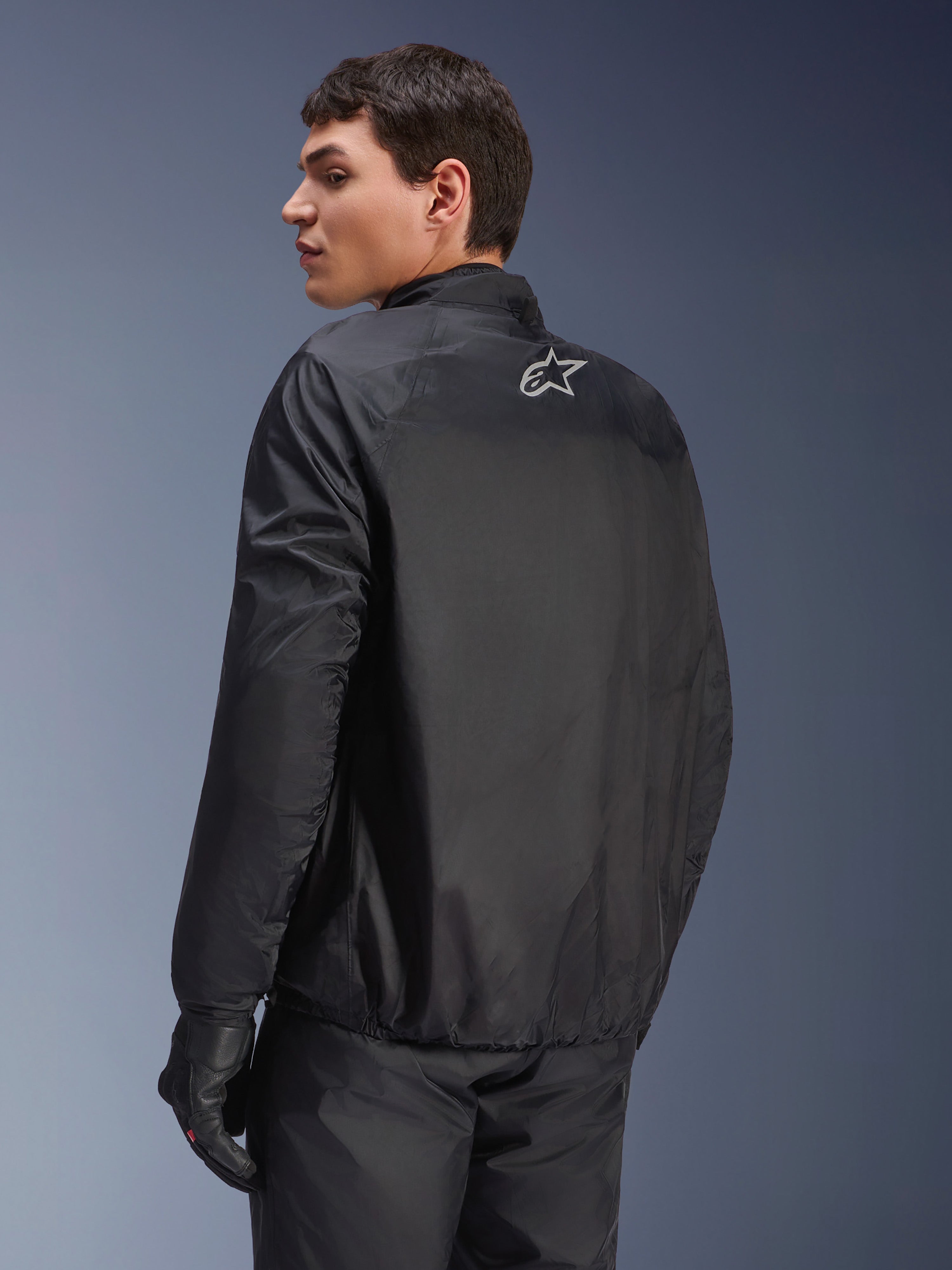 Kurtka Alpinestars Andes Air Drystar®, odpinana membrana wodoodporna w kolorze czarnym, widok z tyłu na męskim modelu, małe białe logo Alpinestars w górnej części pleców, czarne rękawice motocyklowe