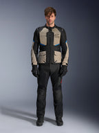 Model ubrany w kurtkę Alpinestars Andes Air Drystar®, motocyklowa kurtka turystyczna, kolor Black Laurel Gray i Bright Blue, zestawiona z pasującymi czarnymi spodniami motocyklowymi i rękawicami, z rozległymi panelami wentylacyjnymi z siatki na klatce piersiowej i rękawach do turystyki przygodowej w ciepłe dni.