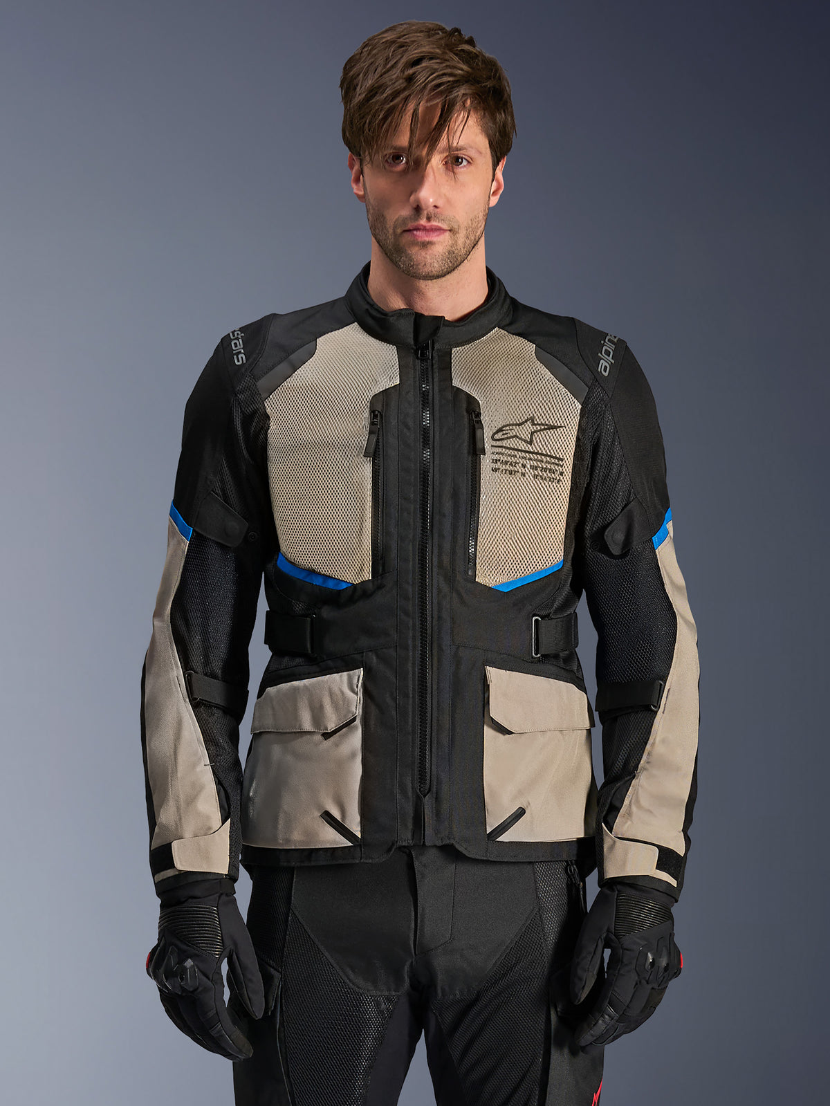 Kurtka Alpinestars Andes Air Drystar, motocyklowa kurtka turystyczna adventure, czarna, szara Laurel Gray i jaskrawoniebieska, noszona przez modela w czarnych rękawicach, z dużymi siateczkowymi panelami na klatce piersiowej dla przepływu powietrza, przednie kieszenie cargo i niebieskie akcenty, ochronna odzież motocyklowa