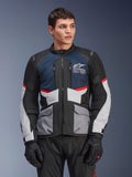 Alpinestars Andes Air Drystar® Jacket, kurtka motocyklowa turystyczna, ciemnoniebieska, czarna i jasnoszara z czerwonymi akcentami, noszona przez modela w czarnych rękawicach, siatkowe panele wentylacyjne i przednie kieszenie użytkowe, nowoczesna odzież typu adventure i szosowa