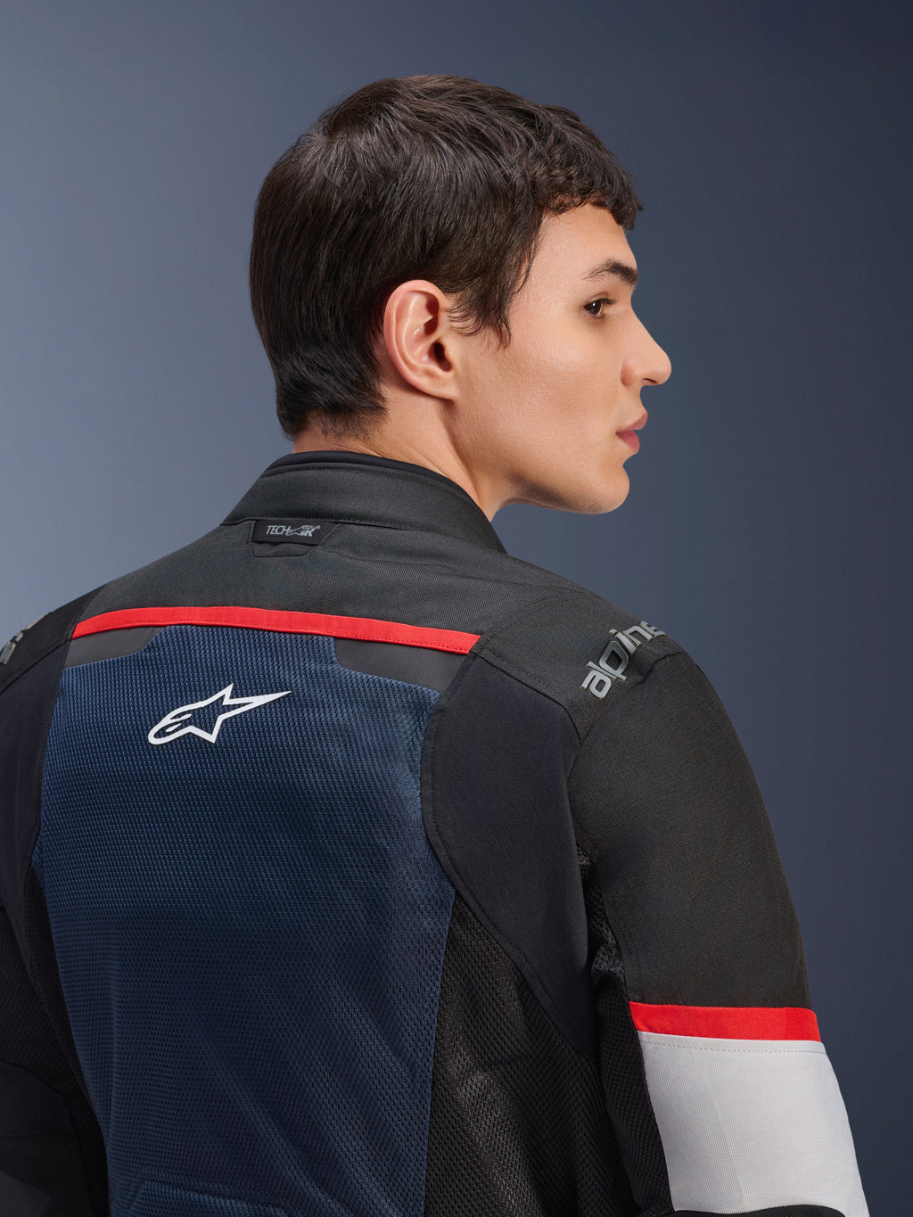Kurtka Alpinestars Andes Air Drystar®, Deep Blue Black i Ice Gray, zbliżenie na tył na modelu, z oddychającym panelem z siatki z białym logo gwiazdy, czerwonymi akcentami i brandingiem Tech-Air® na kołnierzu, turystyczna odzież motocyklowa na dwie pory roku