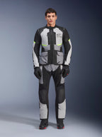 Kurtka Alpinestars Andes Air Drystar® w kolorze Ice Gray, Dark Gray i czarnym, noszona przez modela z dopasowanymi spodniami i rękawicami motocyklowymi, turystyczny design adventure z dużymi przednimi kieszeniami i fluorescencyjnymi żółtymi akcentami, widok z przodu w studio