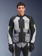 Motocyklista w kurtce Alpinestars Andes Air Drystar® w kolorach Ice Gray, Dark Gray i czarnym, z neonowymi żółtymi akcentami i siatkowymi panelami wentylacyjnymi, zestawionej z dopasowanymi spodniami i rękawicami motocyklowymi, odzież adventure touring