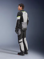 Motocyklista w kurtce i spodniach Alpinestars Andes Air Drystar®, odzież adventure touring w kolorze Ice Gray Dark Gray Black z neonowożółtymi akcentami, obszerne panele z siatki zapewniające przepływ powietrza, logo Alpinestars na plecach, czarne rękawice i buty motocyklowe.