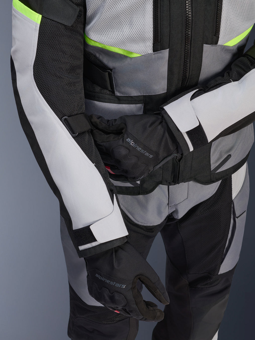 Kurtka Alpinestars Andes Air Drystar®, motocyklowa kurtka turystyczna, jasnoszara i ciemnoszara z neonowożółtymi akcentami, zbliżenie na panele z siatki i paski regulacyjne, noszona z czarnymi rękawicami Alpinestars