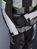 Kurtka Alpinestars Andes Air Drystar®, motocyklowa kurtka turystyczna, jasnoszara i ciemnoszara z neonowożółtymi akcentami, zbliżenie na panele z siatki i paski regulacyjne, noszona z czarnymi rękawicami Alpinestars