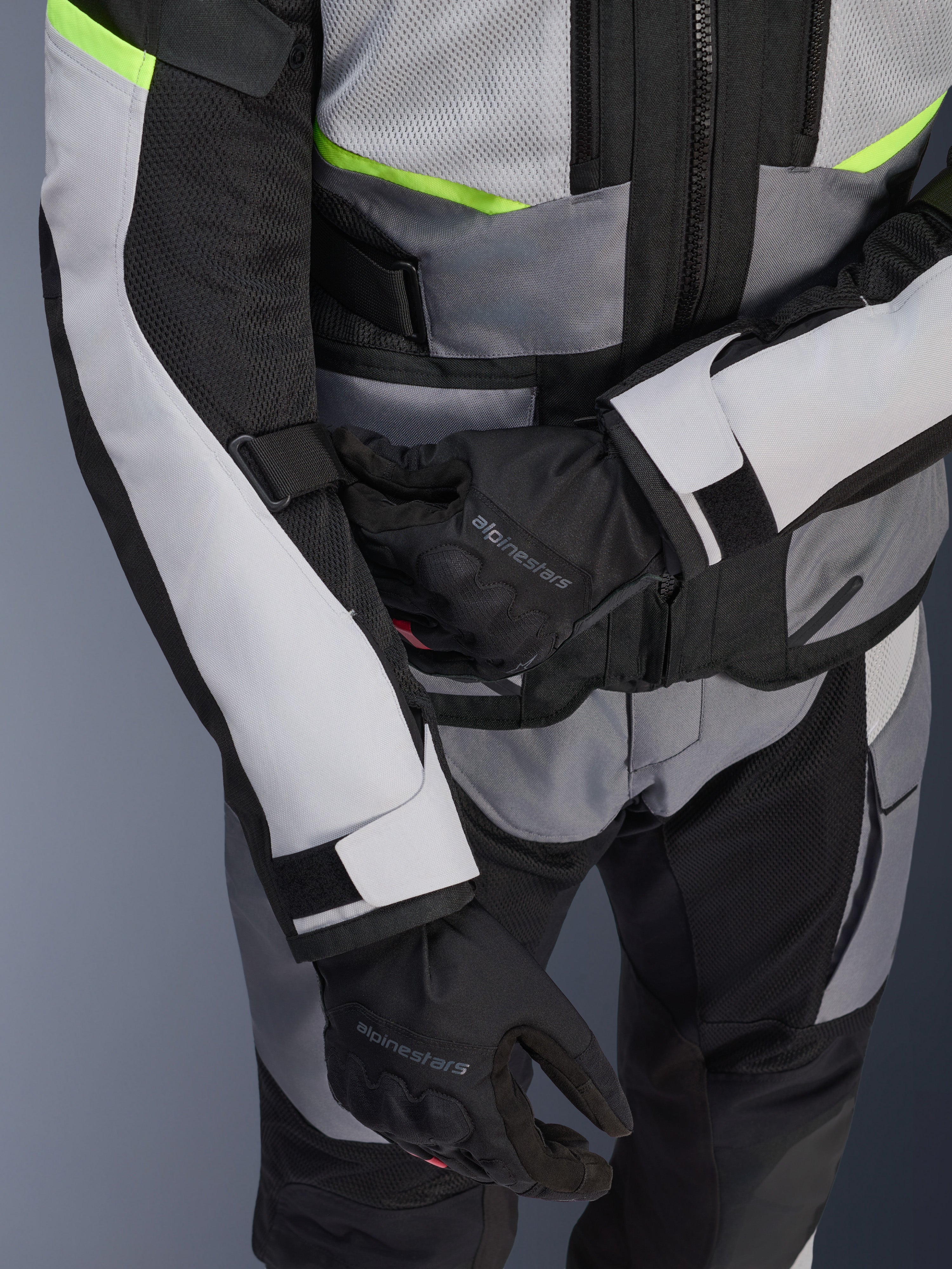 Kurtka Alpinestars Andes Air Drystar®, motocyklowa kurtka turystyczna, jasnoszara i ciemnoszara z neonowożółtymi akcentami, zbliżenie na panele z siatki i paski regulacyjne, noszona z czarnymi rękawicami Alpinestars