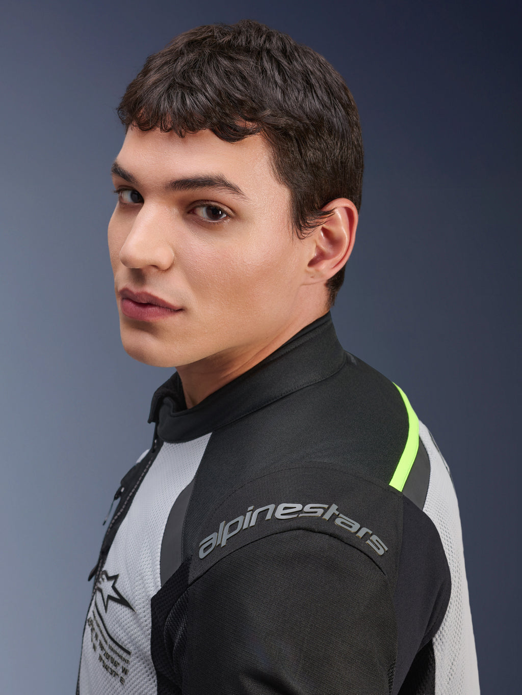 Zbliżenie na modela w kurtce Alpinestars Andes Air Drystar® w kolorach Ice Gray, Dark Gray i czarnym, z neonowożółtymi akcentami i panelami z siatki oraz widocznym logo Alpinestars na ramieniu.