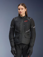 Kurtka Alpinestars Stella Andes Air Drystar, damska kurtka motocyklowa turystyczna, czarna z szarymi akcentami i małym czerwonym logo, z siatkowymi panelami wentylacyjnymi, wysokim kołnierzem i wieloma praktycznymi kieszeniami, noszona wraz z pasującymi rękawicami i spodniami motocyklowymi