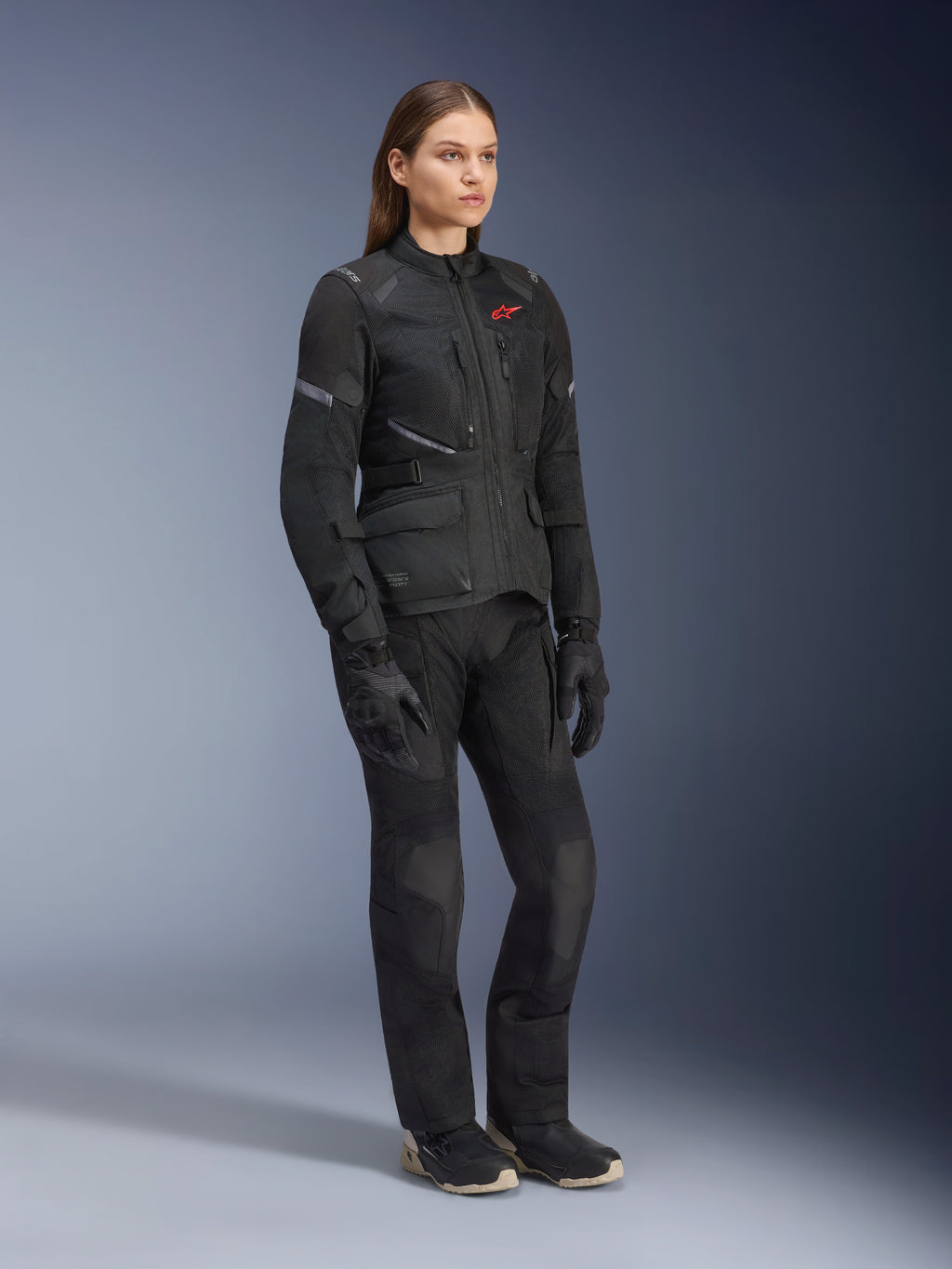 Kobieta ubrana w kurtkę Alpinestars Stella Andes Air Drystar®, czarna tekstylna kurtka turystyczna adventure, noszona z pasującymi czarnymi spodniami i rękawicami, z dużymi panelami wentylacyjnymi z siatki i czerwonym logo, dopasowany strój do jazdy motocyklem dla kobiet