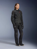 Kobieta ubrana w kurtkę Alpinestars Stella Andes Air Drystar®, czarna tekstylna kurtka turystyczna adventure, noszona z pasującymi czarnymi spodniami i rękawicami, z dużymi panelami wentylacyjnymi z siatki i czerwonym logo, dopasowany strój do jazdy motocyklem dla kobiet