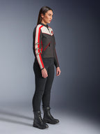 Modelka stojąca profilem w kurtce Alpinestars Stella T-Dyno WR w kolorach czarnym, ecru i jaskrawoczerwonym, z pasami wyścigowymi na rękawach i logo gwiazdy, czarne spodnie i sznurowane buty, miejski styl motocyklowy