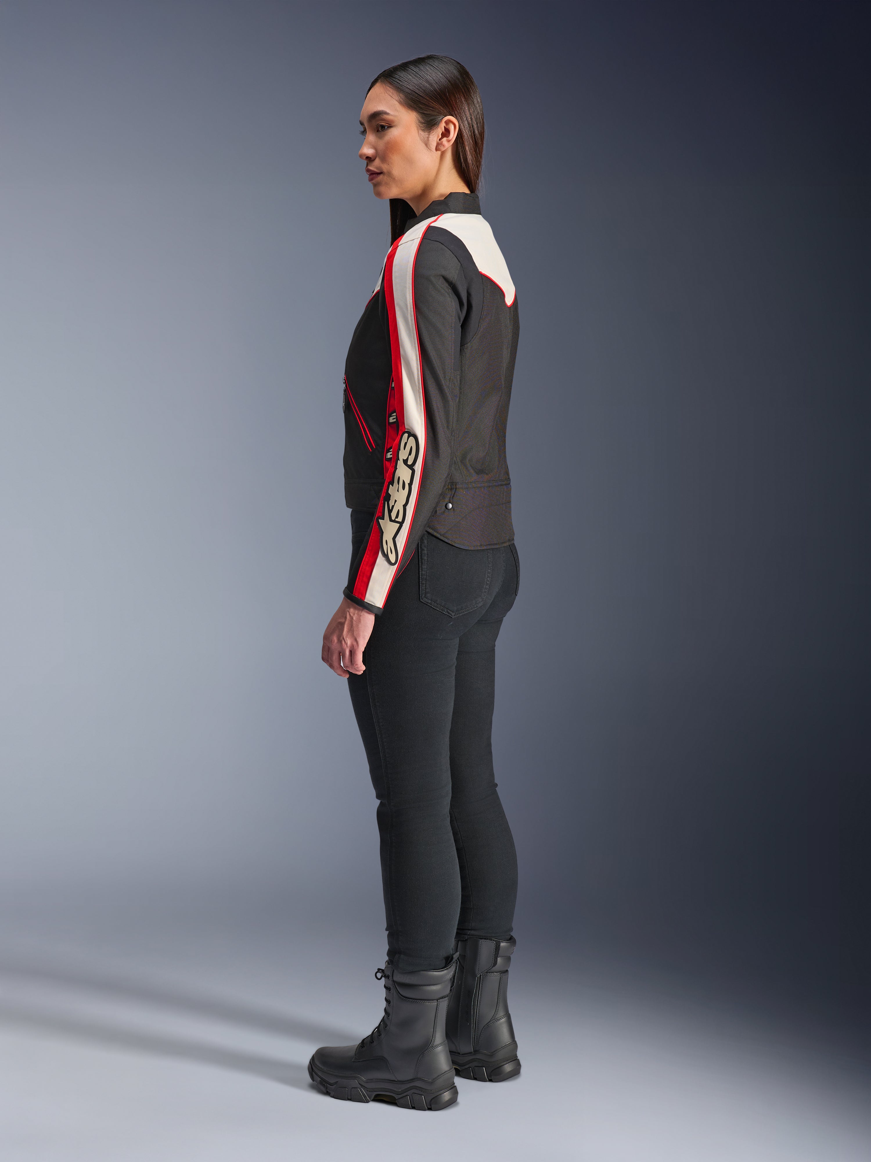 Kurtka Alpinestars Stella T-Dyno WR, damska tekstylna kurtka motocyklowa, czarna, ecru i jaskrawoczerwona, design inspirowany stylem vintage z logo Astars na rękawie, noszona z dopasowanymi czarnymi spodniami i czarnymi butami, krótki motocyklowy krój do jazdy miejskiej
