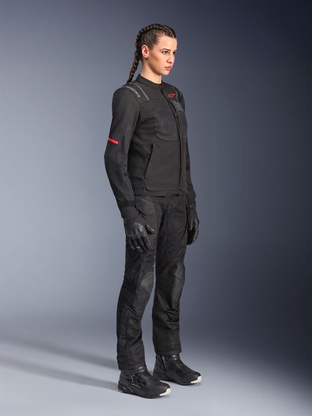 Motocyklistka ubrana w czarne spodnie Alpinestars Stella Andes Air Drystar®, tekstylne spodnie adventure z siatkowymi panelami wentylacyjnymi, zestawione z pasującą kurtką Stella, rękawicami i butami, tworzące kompletny motocyklowy strój turystyczny.