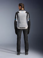 Damska kurtka Alpinestars Stella ST-2 Air, kolor Ice Gray Black, widok z tyłu na modelce, duży jasnoszary siatkowy panel na plecach, czarne rękawy z niebieskimi akcentami, logo Alpinestars na dole pleców, czarne techniczne spodnie i buty motocyklowe, letnia odzież turystyczna