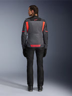 Widok od tyłu modelki ubranej w damską kurtkę Alpinestars Stella ST-2 Air w kolorach Deep Gray i Dark Gray z akcentami Fluo Coral, z dużymi siatkowymi panelami wentylacyjnymi na plecach i odblaskowymi detalami logo, w połączeniu z czarnymi spodniami motocyklowymi i rękawicami.
