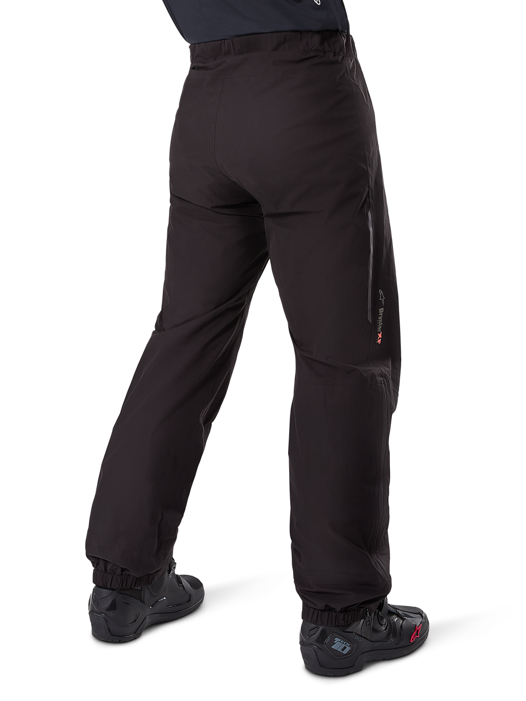Podpinka Alpinestars Amt-8 Stretch Drystar® XF, czarna, widok z tyłu przedstawiający wodoodporną warstwę założoną na czarne buty motocyklowe, logo Drystar XF na dole nogawki, elastyczne mankiety, lekki i rozciągliwy materiał do turystyki przygodowej.