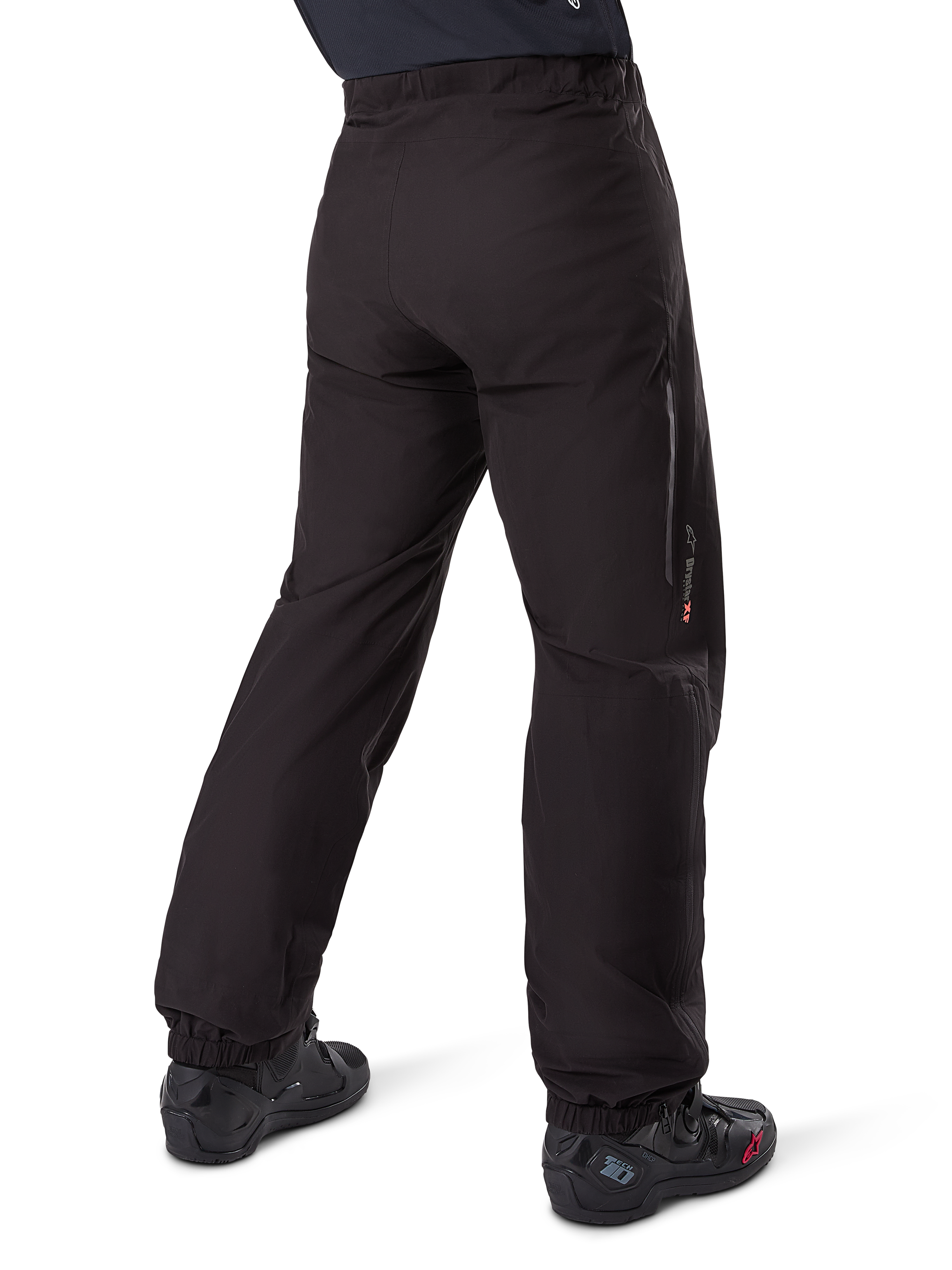 Podpinka Alpinestars Amt-8 Stretch Drystar® XF, czarna, widok z tyłu przedstawiający wodoodporną warstwę założoną na czarne buty motocyklowe, logo Drystar XF na dole nogawki, elastyczne mankiety, lekki i rozciągliwy materiał do turystyki przygodowej.