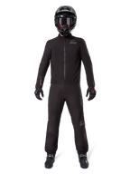 Motocyklista ubrany w podszewkę spodni Alpinestars AMT-8 Stretch Drystar® XF i pasującą kurtkę, czarny wodoodporny i wiatroszczelny strój techniczny, czarny kask, rękawice i buty, elegancki design adventure touring
