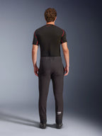 Spodnie Alpinestars Aeroshell, sportowe motocyklowe spodnie softshellowe typu crossover, czarne, widok z tyłu, zestawione z czarną warstwą bazową z krótkim rękawem, o dopasowanym kroju, profilowane kolana i białe logo Astars na dole lewej nogawki.