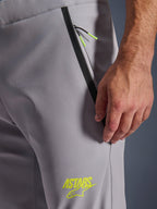 Spodnie Alpinestars Aeroshell, kolor średnioszary z jaskrawożółtymi akcentami, zbliżenie na przednią kieszeń zapinaną na zamek z czarnym wykończeniem i jaskrawożółtymi sznurkami, żółte logo ASTARS na udzie, elastyczny materiał softshell do jazdy motocyklem