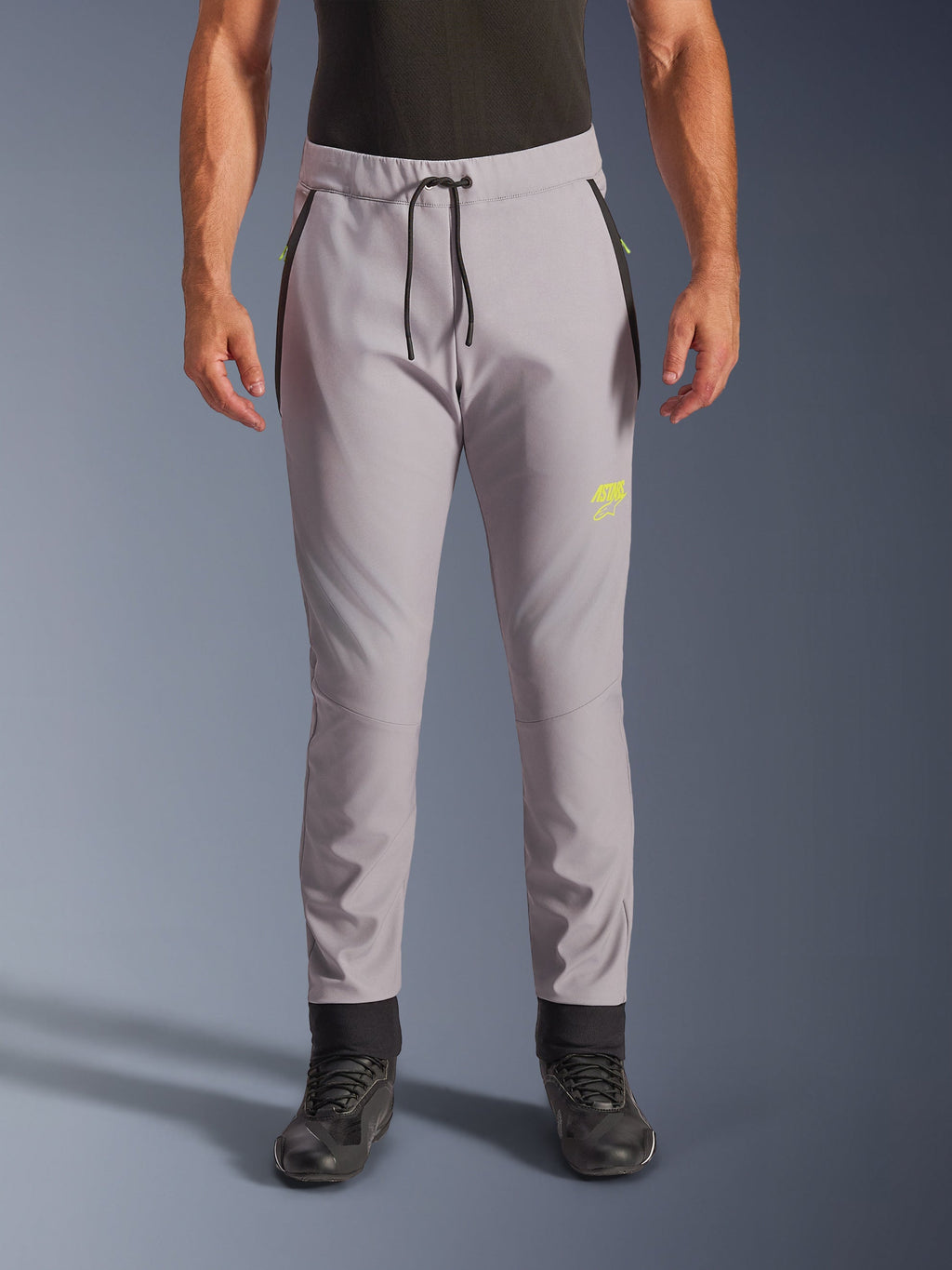 Alpinestars Aeroshell Pants, motocyklowe spodnie softshellowe typu crossover, szare i jaskrawożółte, czarny sznurek w pasie i dopasowane ściągacze przy kostkach, żółte logo na lewym udzie, profilowane kolana, sportowa sylwetka typu jogger