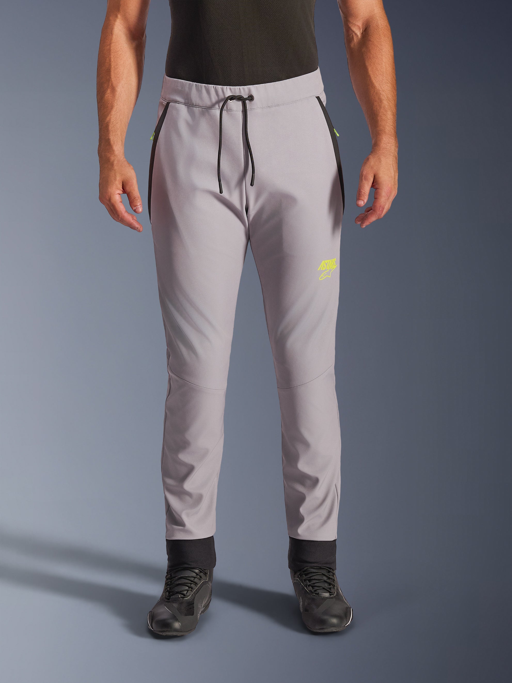 Alpinestars Aeroshell Pants, motocyklowe spodnie softshellowe typu crossover, szare i jaskrawożółte, czarny sznurek w pasie i dopasowane ściągacze przy kostkach, żółte logo na lewym udzie, profilowane kolana, sportowa sylwetka typu jogger