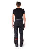 Alpinestars Hyde Xt Drystar® Pants, Adventure Touring Motorcycle Pants, Black and Bright Red, rear view of a rider wearing the pants and a black base layer, featuring a red star logo on the left leg and grey branding on the waistband.