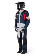 Spodnie Alpinestars St-1 Waterproof, spodnie turystyczne adventure, ciemnoniebieskie, czarne i jaskrawoczerwone, noszone z pasującą kurtką turystyczną, czarnym kaskiem, rękawicami i butami, z jasnoszarymi panelami, czerwonymi akcentami i brandingiem Alpinestars, zaprojektowane do jazdy w każdych warunkach pogodowych.