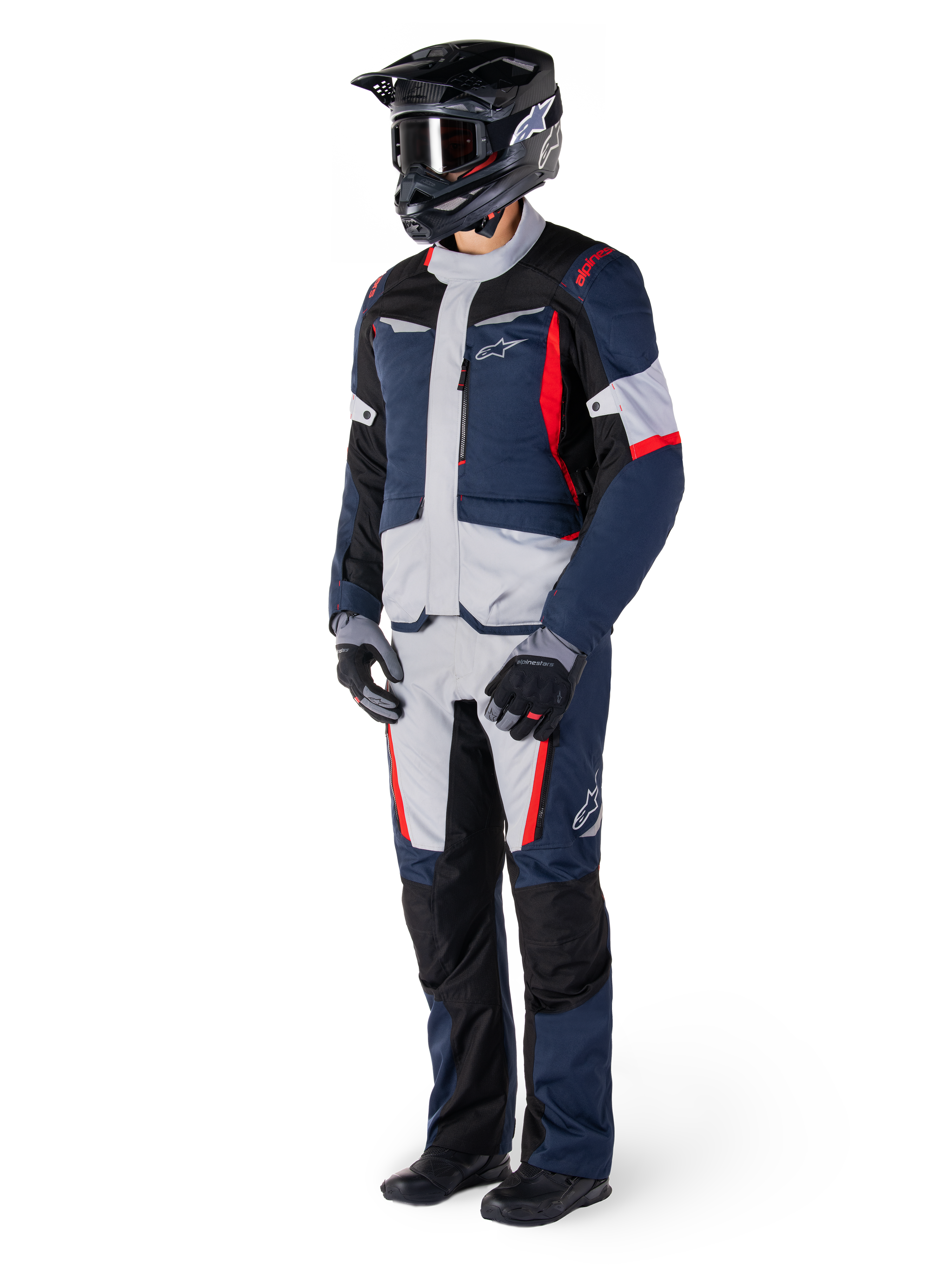 Spodnie Alpinestars St-1 Waterproof, spodnie turystyczne adventure, ciemnoniebieskie, czarne i jaskrawoczerwone, noszone z pasującą kurtką turystyczną, czarnym kaskiem, rękawicami i butami, z jasnoszarymi panelami, czerwonymi akcentami i brandingiem Alpinestars, zaprojektowane do jazdy w każdych warunkach pogodowych.