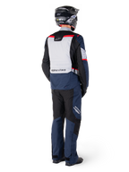 Widok z tyłu motocyklisty ubranego w spodnie Alpinestars ST-1 Waterproof i pasującą kurtkę w kolorze granatowo-czarnym z jaskrawoczerwonymi akcentami, odzież adventure touring z panelami tekstylnymi i odblaskowymi elementami, czarny kask i buty