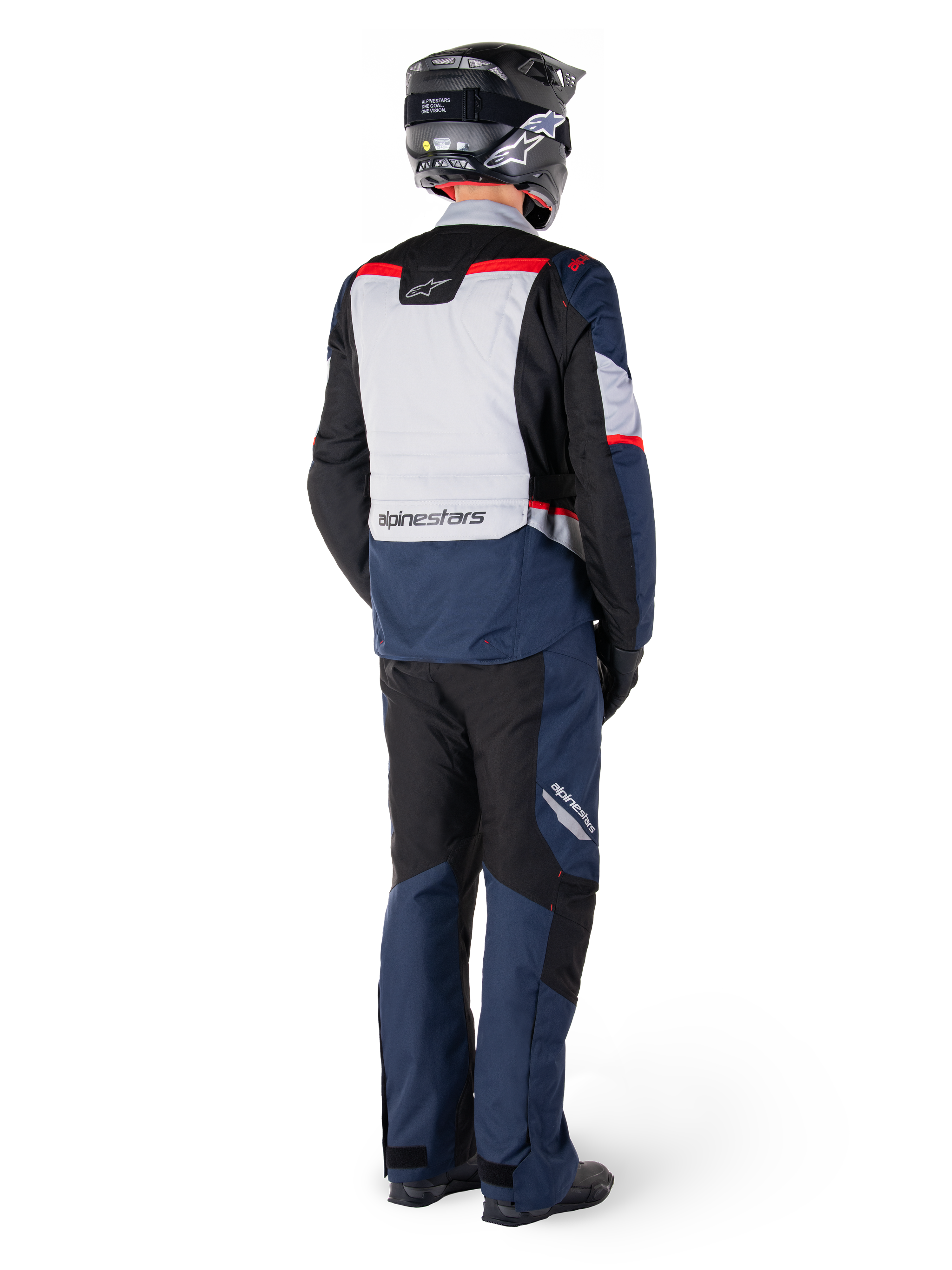 Widok z tyłu motocyklisty ubranego w spodnie Alpinestars ST-1 Waterproof i pasującą kurtkę w kolorze granatowo-czarnym z jaskrawoczerwonymi akcentami, odzież adventure touring z panelami tekstylnymi i odblaskowymi elementami, czarny kask i buty