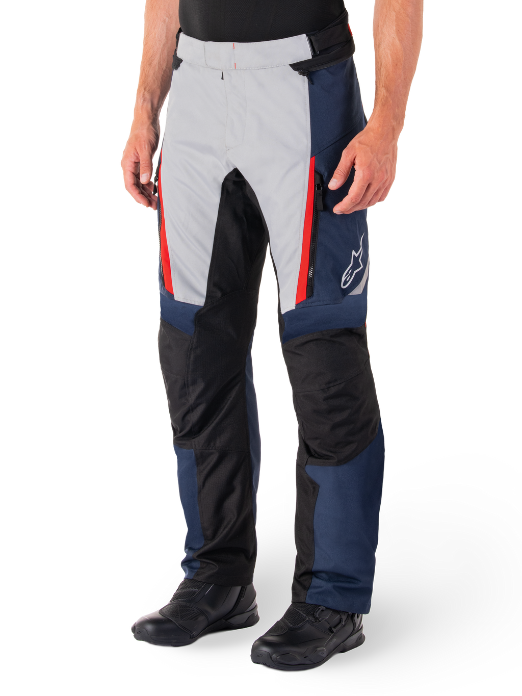 Alpinestars St-1 Waterproof Pants, motocyklowe spodnie turystyczne, ciemnoniebieskie, czarne i jaskrawoczerwone, jasnoszare panele przednie z czerwonymi akcentami przy zamkach, czarne wzmocnione sekcje na kolanach, białe logo Alpinestars z boku, noszone z czarnymi butami motocyklowymi