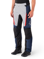 Alpinestars St-1 Waterproof Pants, motocyklowe spodnie turystyczne, ciemnoniebieskie, czarne i jaskrawoczerwone, jasnoszare panele przednie z czerwonymi akcentami przy zamkach, czarne wzmocnione sekcje na kolanach, białe logo Alpinestars z boku, noszone z czarnymi butami motocyklowymi