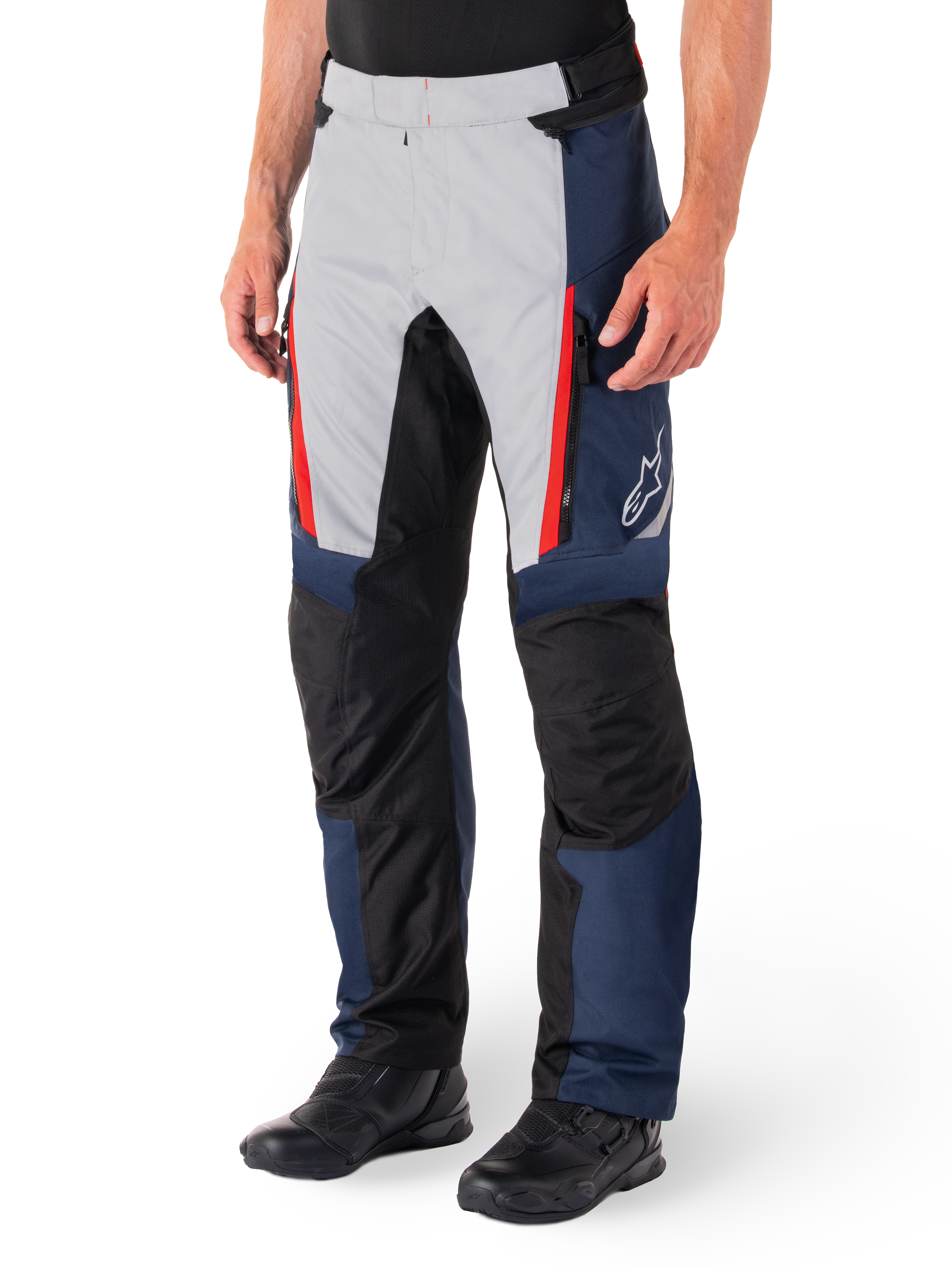 Alpinestars St-1 Waterproof Pants, motocyklowe spodnie turystyczne, ciemnoniebieskie, czarne i jaskrawoczerwone, jasnoszare panele przednie z czerwonymi akcentami przy zamkach, czarne wzmocnione sekcje na kolanach, białe logo Alpinestars z boku, noszone z czarnymi butami motocyklowymi