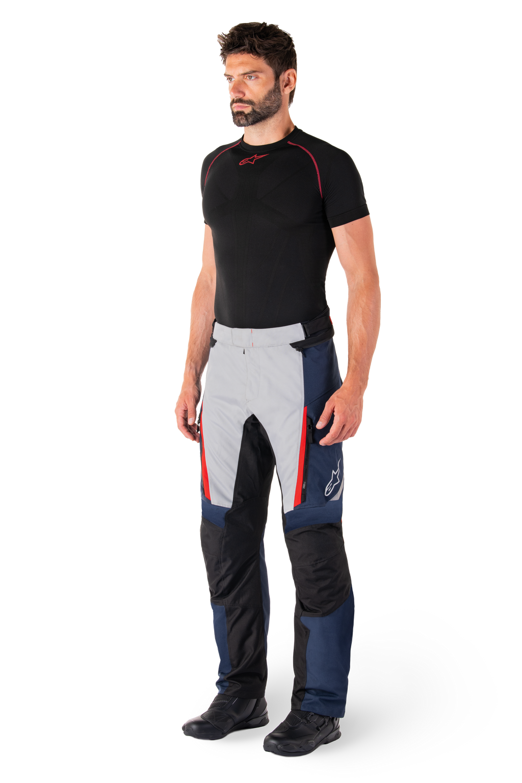 Alpinestars St-1 Waterproof Pants, motocyklowe spodnie turystyczne, ciemnoniebieskie, czarne i jaskrawoczerwone, noszone przez modela z czarną warstwą bazową i czarnymi butami, posiadają kieszenie na zamek i logo Alpinestars na nogawce