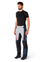 Alpinestars St-1 Waterproof Pants, motocyklowe spodnie turystyczne, ciemnoniebieskie, czarne i jaskrawoczerwone, noszone przez modela z czarną warstwą bazową i czarnymi butami, posiadają kieszenie na zamek i logo Alpinestars na nogawce