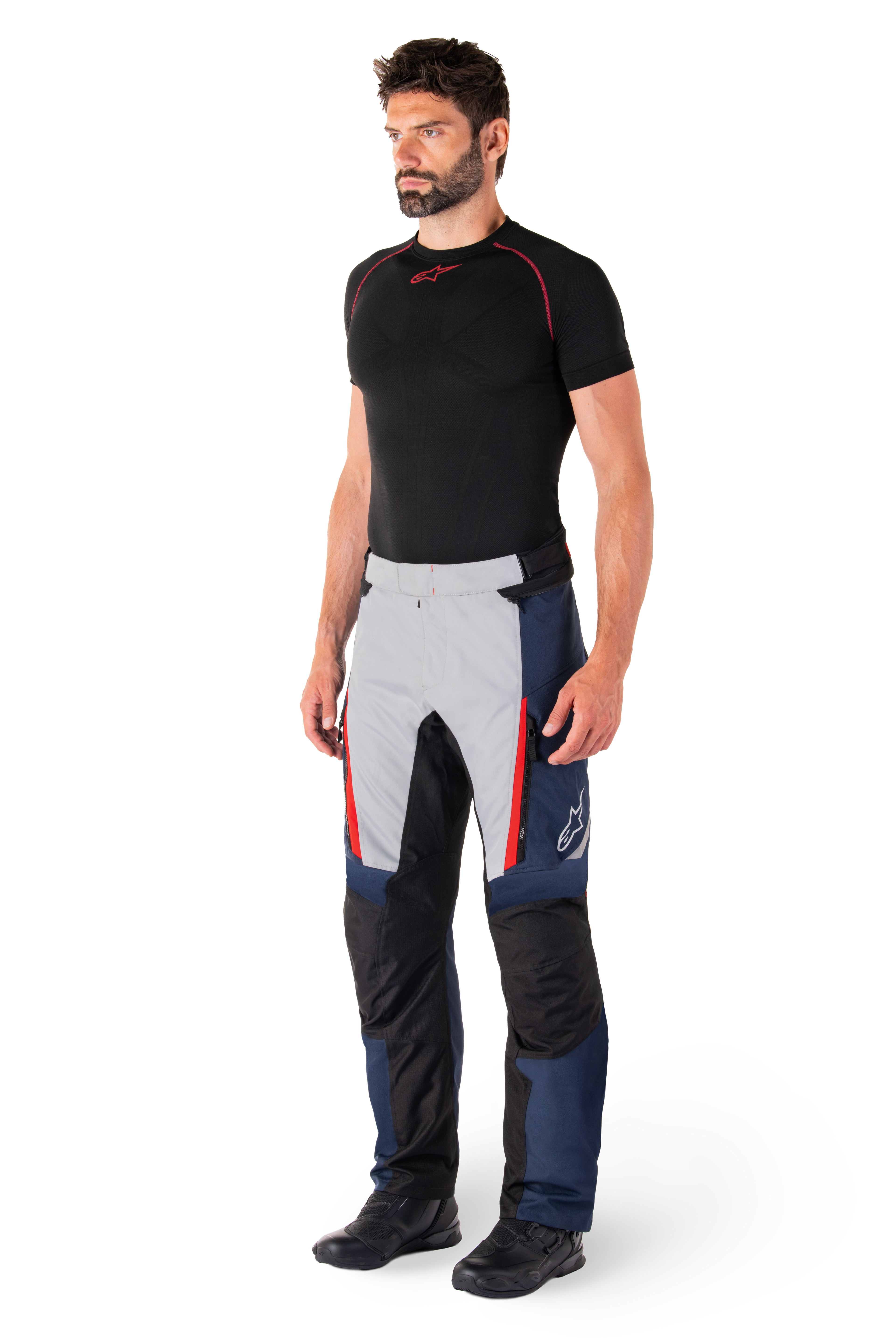 Alpinestars St-1 Waterproof Pants, motocyklowe spodnie turystyczne, ciemnoniebieskie, czarne i jaskrawoczerwone, noszone przez modela z czarną warstwą bazową i czarnymi butami, posiadają kieszenie na zamek i logo Alpinestars na nogawce