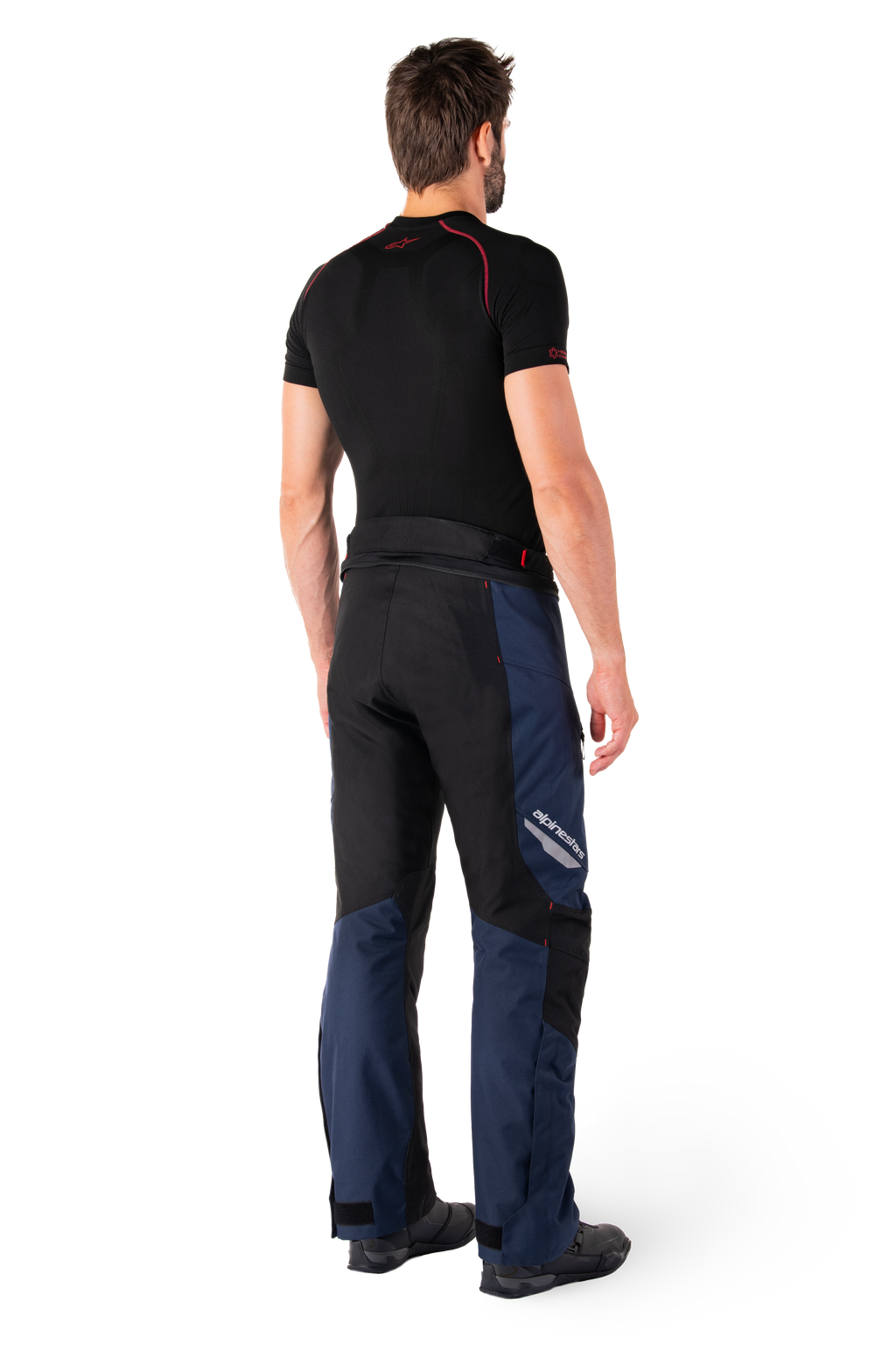 Spodnie Alpinestars St-1 Waterproof, spodnie adventure touring, granatowo-czarne i jaskrawoczerwone, widok z tyłu z boku, noszone z czarną warstwą bazową z krótkim rękawem i czarnymi butami motocyklowymi, smukła konstrukcja z odblaskowym logo i czerwonymi akcentami