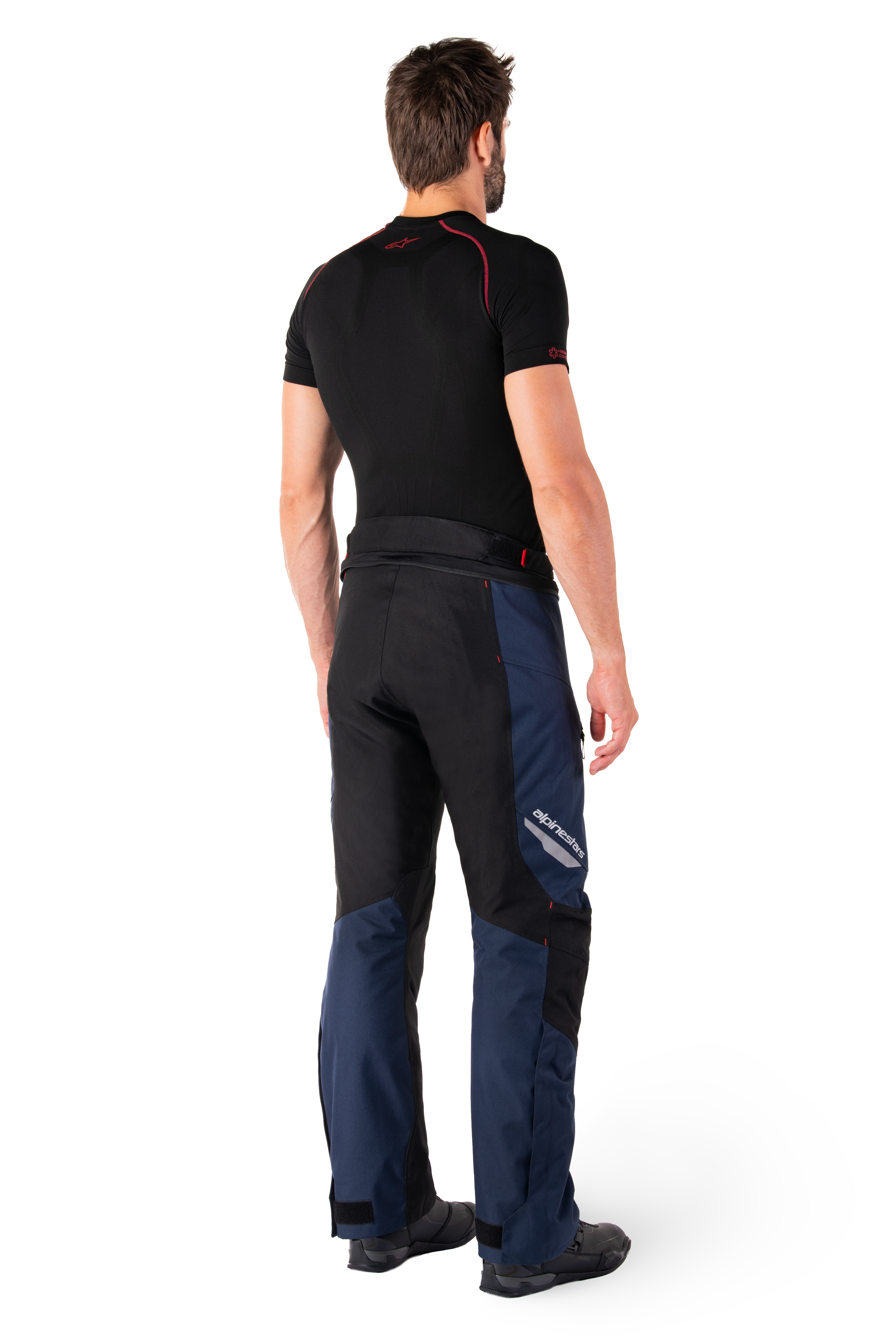 Spodnie Alpinestars St-1 Waterproof, spodnie adventure touring, granatowo-czarne i jaskrawoczerwone, widok z tyłu z boku, noszone z czarną warstwą bazową z krótkim rękawem i czarnymi butami motocyklowymi, smukła konstrukcja z odblaskowym logo i czerwonymi akcentami