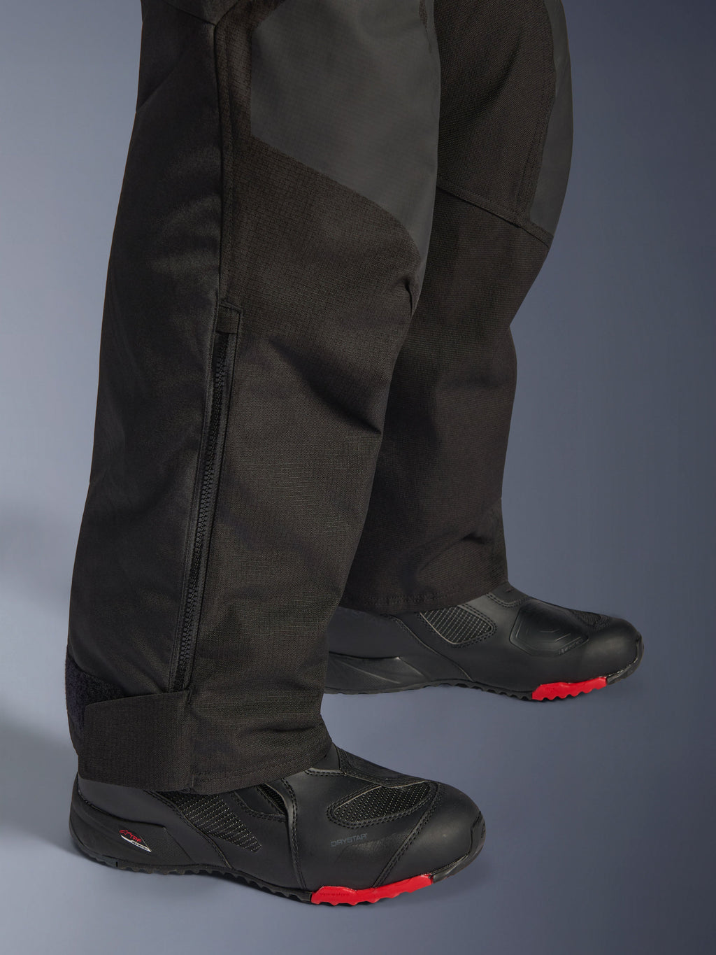 Alpinestars Andes V4 Drystar® Pants - Short, czarne, zbliżenie na detale dolnej części nogawki przedstawiające konstrukcję tekstylną, pionowy zamek wentylacyjny oraz regulowane mankiety na kostkach, noszone z czarnymi butami motocyklowymi