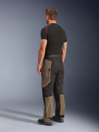 Alpinestars Cusco Drystar® Pants, przygodowe spodnie motocyklowe, kolor Walnut Black, widok z tyłu z boku, zestawione z czarną warstwą bazową i butami, wzmocnione panele tekstylne, kieszenie cargo na zamki na udach, ergonomiczny krój turystyczny.