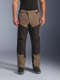 Alpinestars Cusco Drystar® Pants, motocyklowe spodnie turystyczne adventure touring, orzechowo-czarne z pomarańczowymi akcentami, widok z przodu na modelu, techniczna konstrukcja tekstylna, kieszenie cargo i zamki wentylacyjne, zestawione z czarnymi butami motocyklowymi